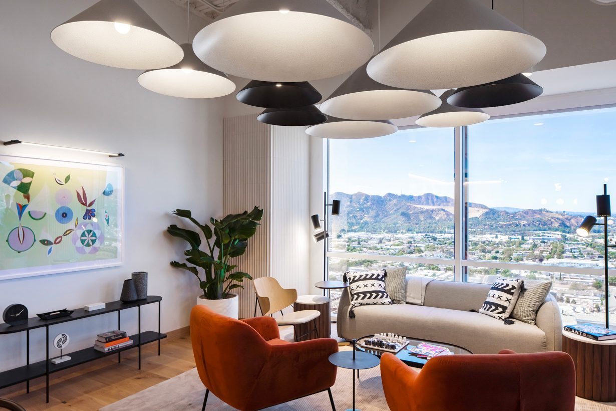 Floor-to-ceiling windows, ample greenery, and chic light fixtures add warmth and vibrancy to the space.